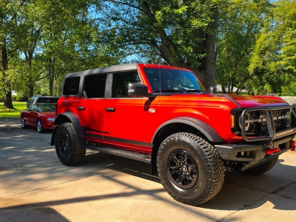 Red Ford Bronco parked outside with black wheels and trim.