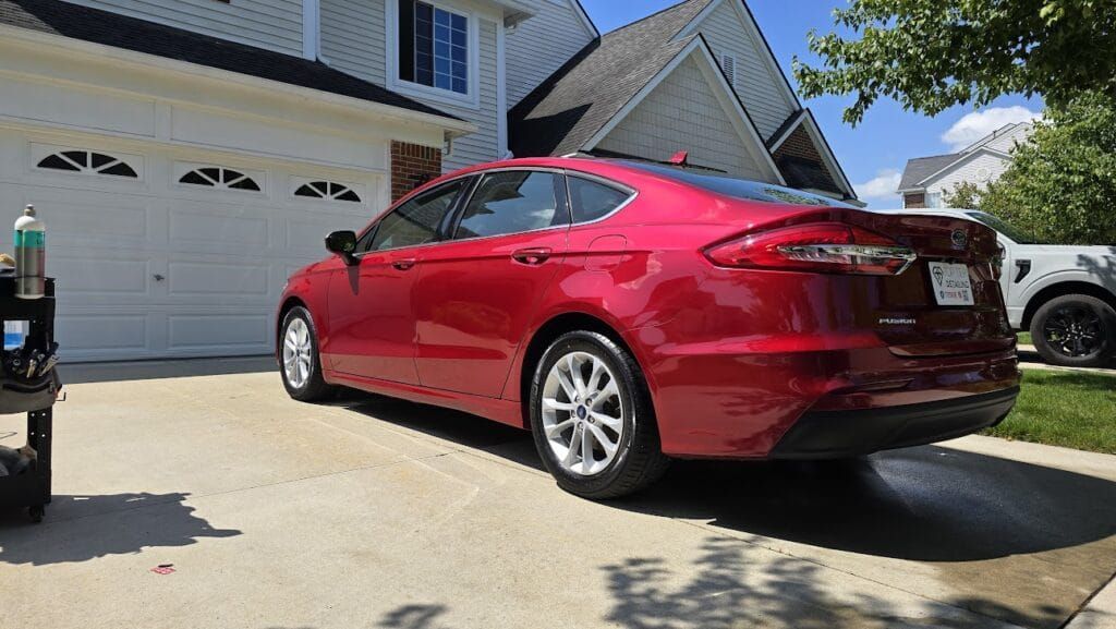 Red car parked on a driveway in front of a house with a white garage door on a sunny day.