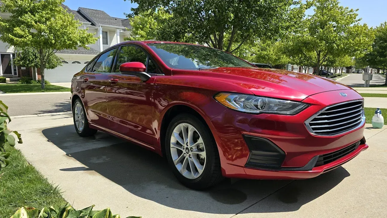 Red Ford Fusion sedan parked on a sunny driveway in front of a house.