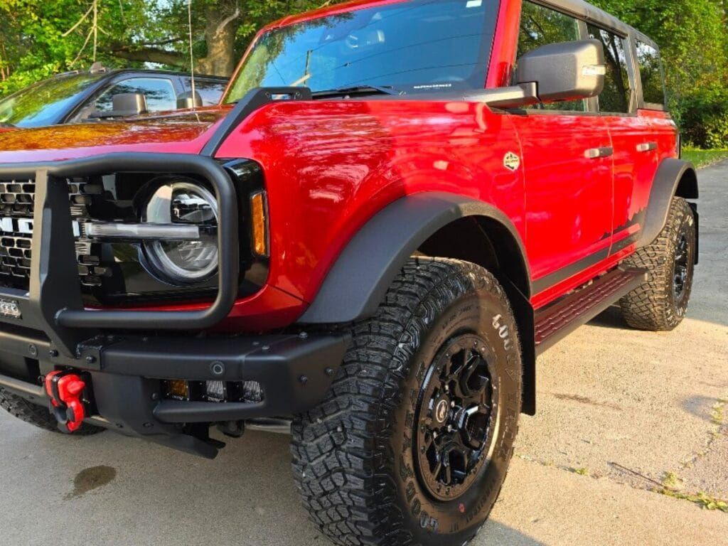 Red Ford Bronco SUV with black accents, large tires, parked outdoors.