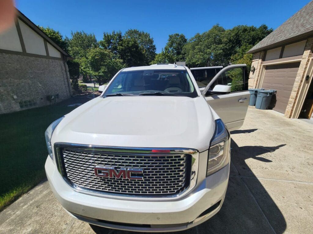 White GMC Yukon SUV parked in a driveway with the door open on a sunny day.