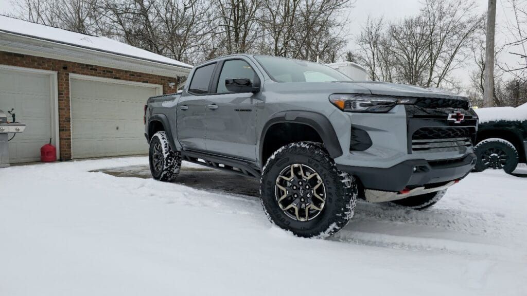 Gray Chevrolet truck parked in snowy driveway in front of a garage.