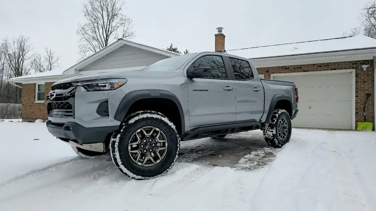 Gray Chevrolet truck parked in snow-covered driveway in front of a house with a white garage.