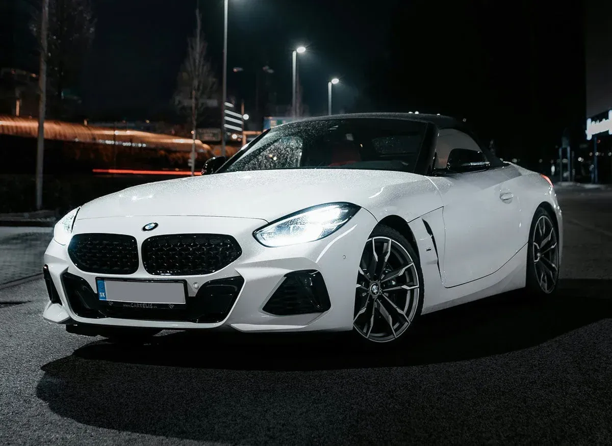 White BMW Z4 roadster at night, headlights on, parked on a dark street.