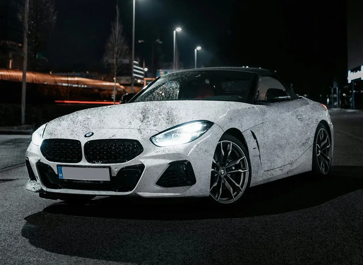 White BMW Z4 roadster on an asphalt road at night, headlights on.