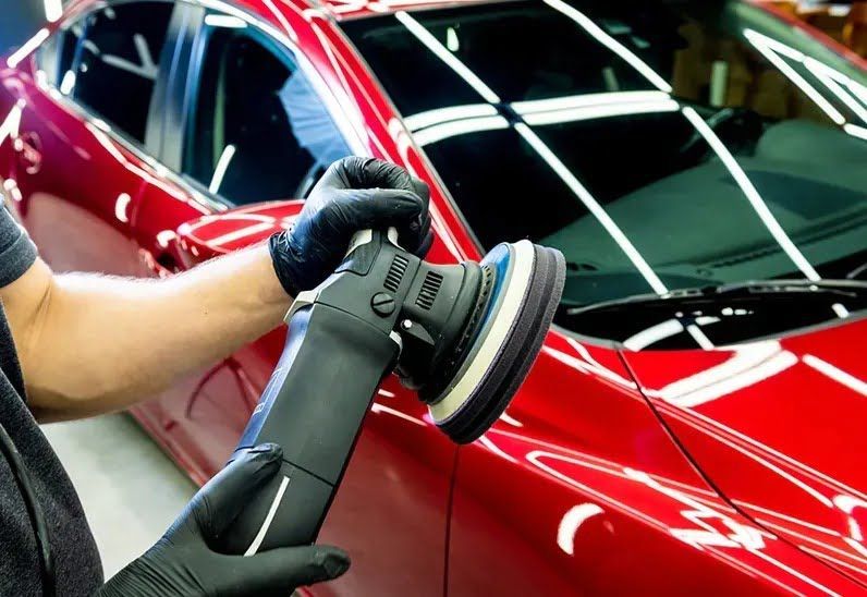 Person in black gloves polishing a red car with a machine in a well-lit setting.