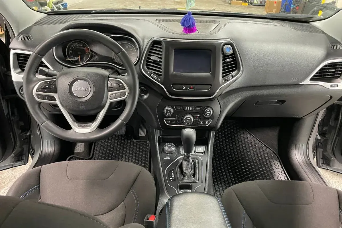 Black Jeep Cherokee interior showing the dashboard, steering wheel, touchscreen, and center console.