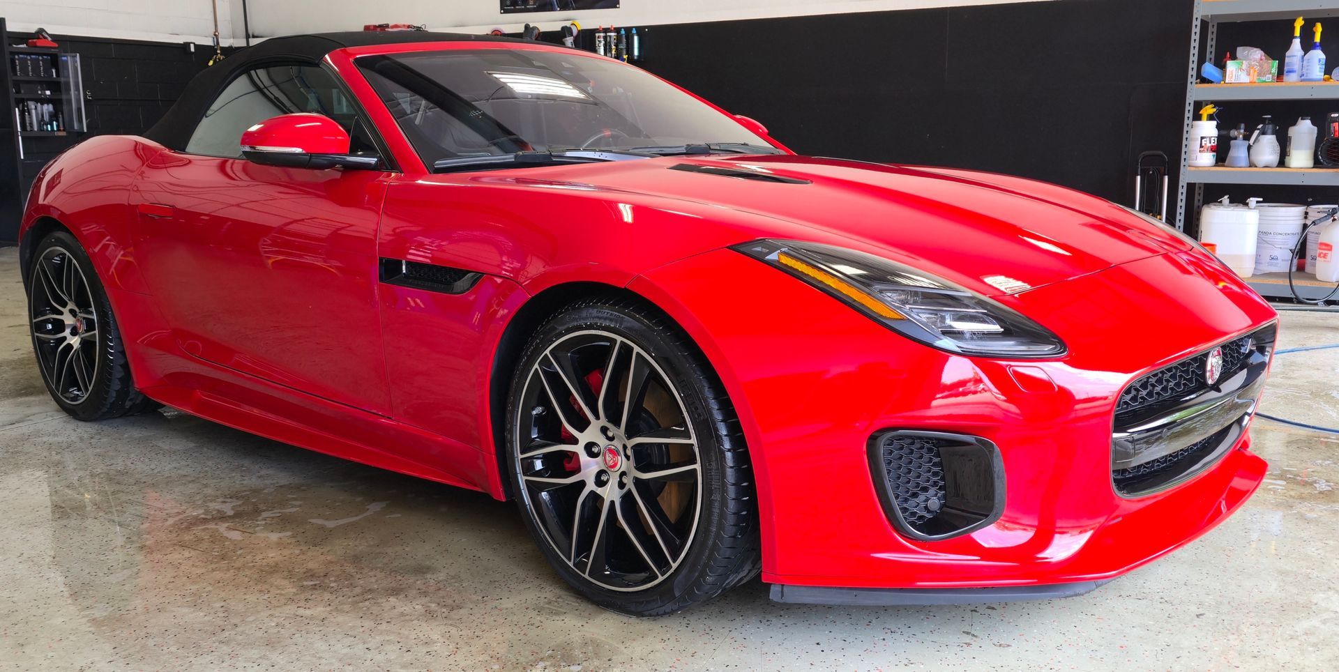 Red Jaguar convertible parked in a garage. Black rims and black interior, glossy finish.