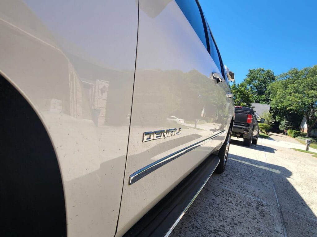 Side view of a tan GMC Denali SUV parked on a driveway on a sunny day.