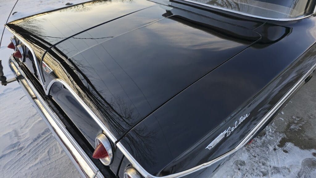 Black classic car, rear view. Shiny black body, chrome trim, and taillights. Snow ground.