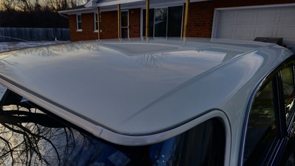 White car roof reflecting sunlight, with a brick house and garage in the background.