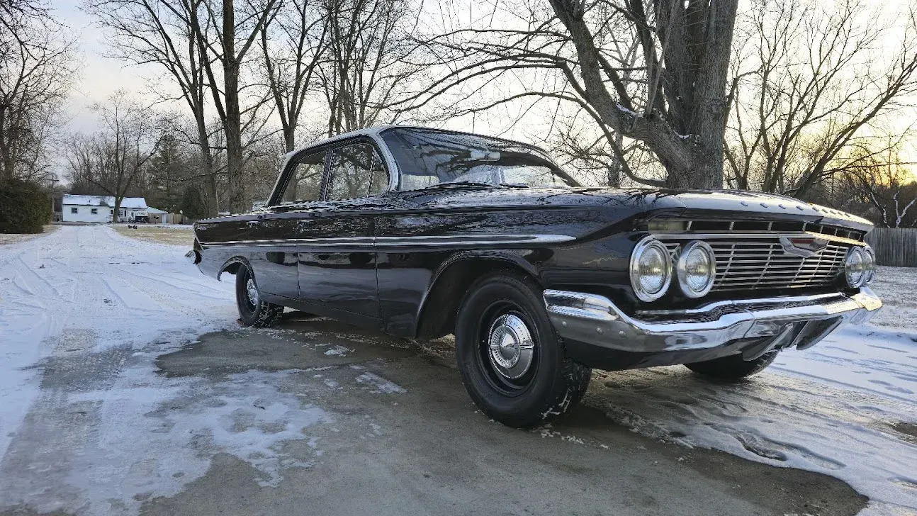 Black classic car with chrome trim in snowy setting.