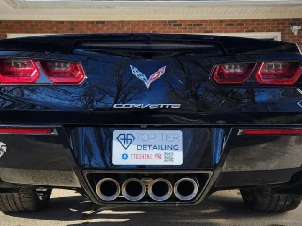 Rear view of a black Corvette with detailing company's license plate and quad exhaust pipes.