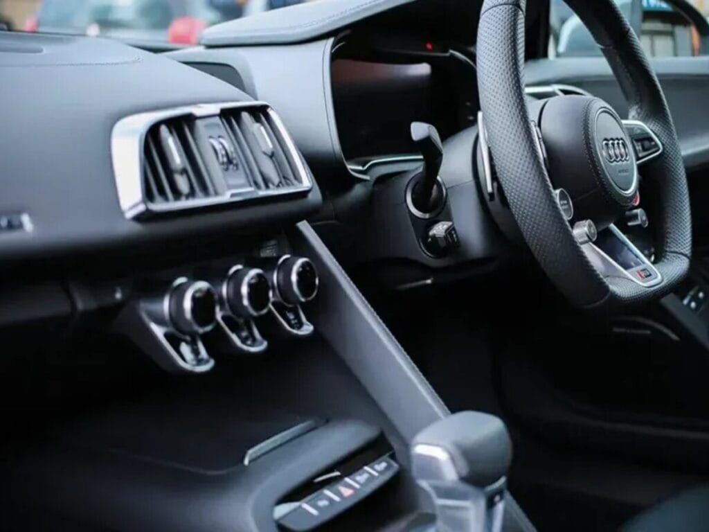 Interior view of a black Audi R8, showing dashboard, steering wheel, air vents, and controls.