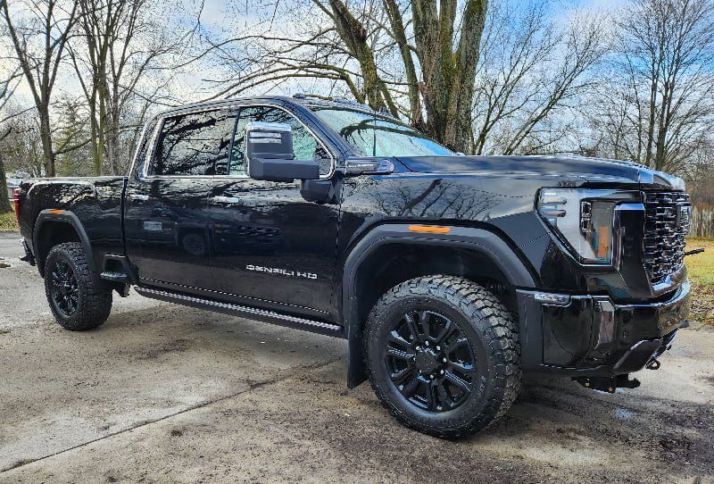 Black GMC Sierra truck parked on a paved surface, overcast sky in background.