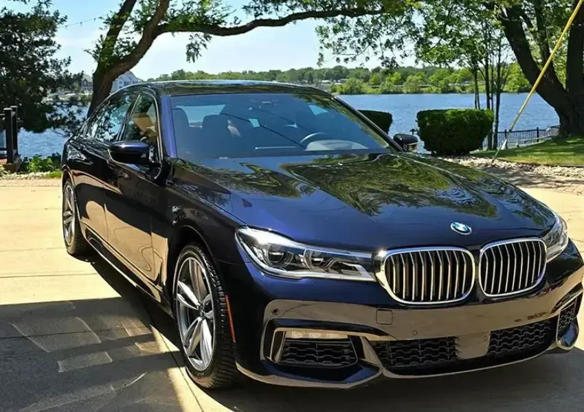 Blue BMW sedan parked outdoors near a body of water, sunny day.
