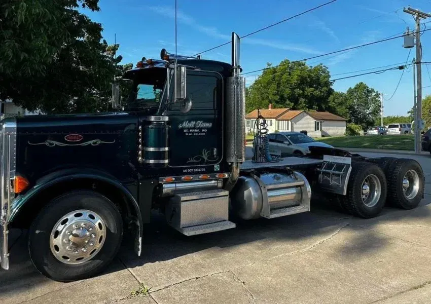 Dark green Peterbilt semi-truck parked on a street, daytime, sunny.