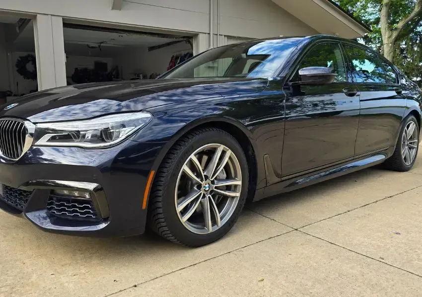Dark blue BMW 7 Series sedan parked on a concrete driveway in front of a garage.