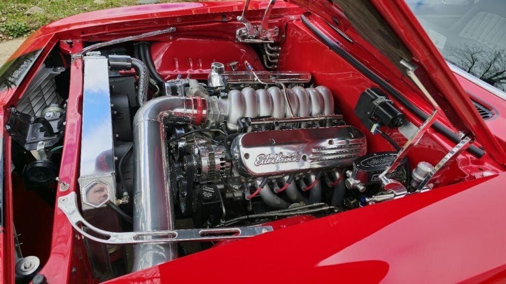 Red car engine bay with a large chrome engine and polished components.