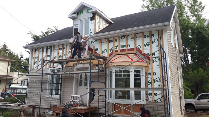 Une maison est en cours de rénovation avec des échafaudages et un camion garé devant.