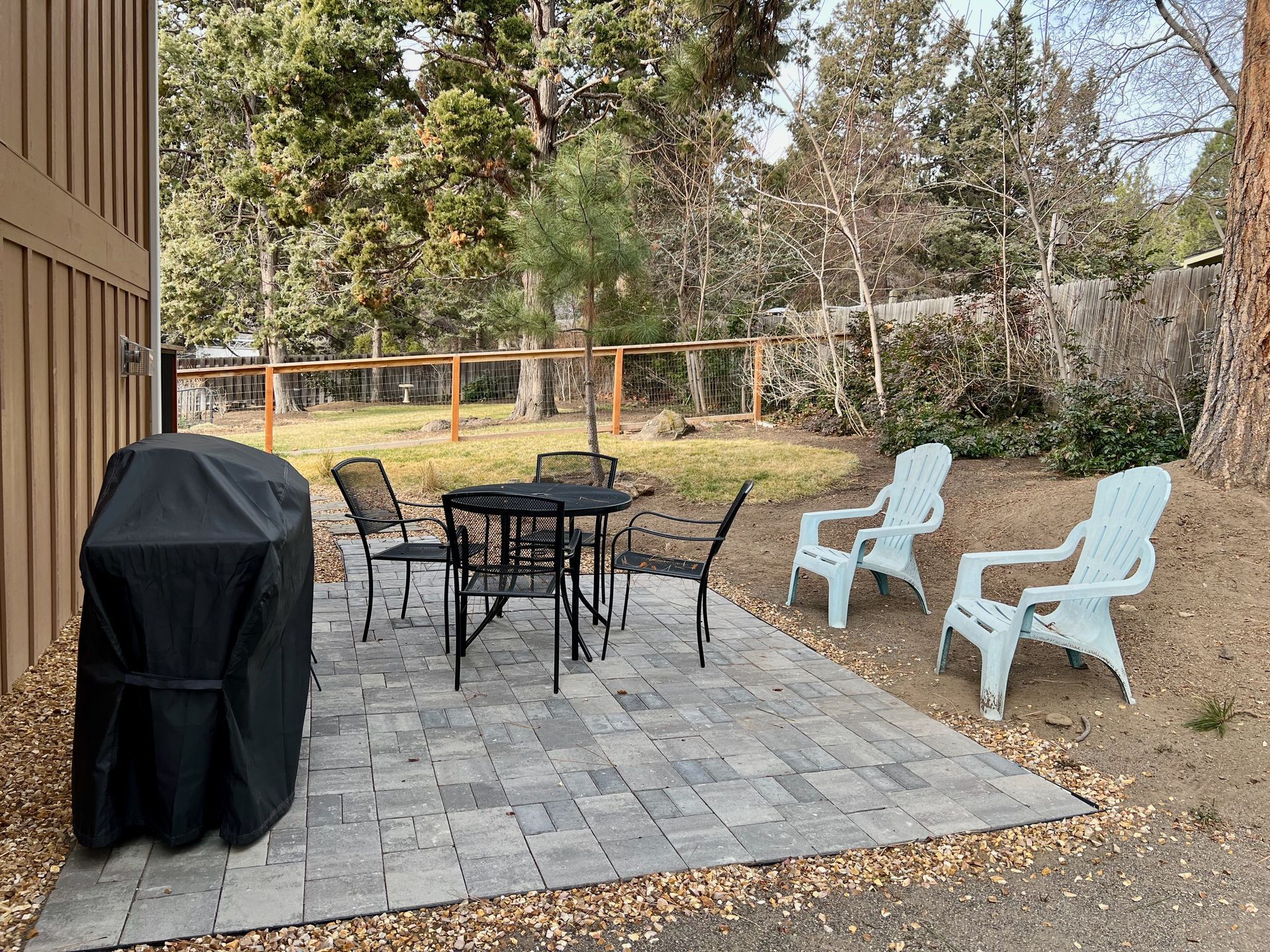 Patio with grill, table, chairs, and trees.