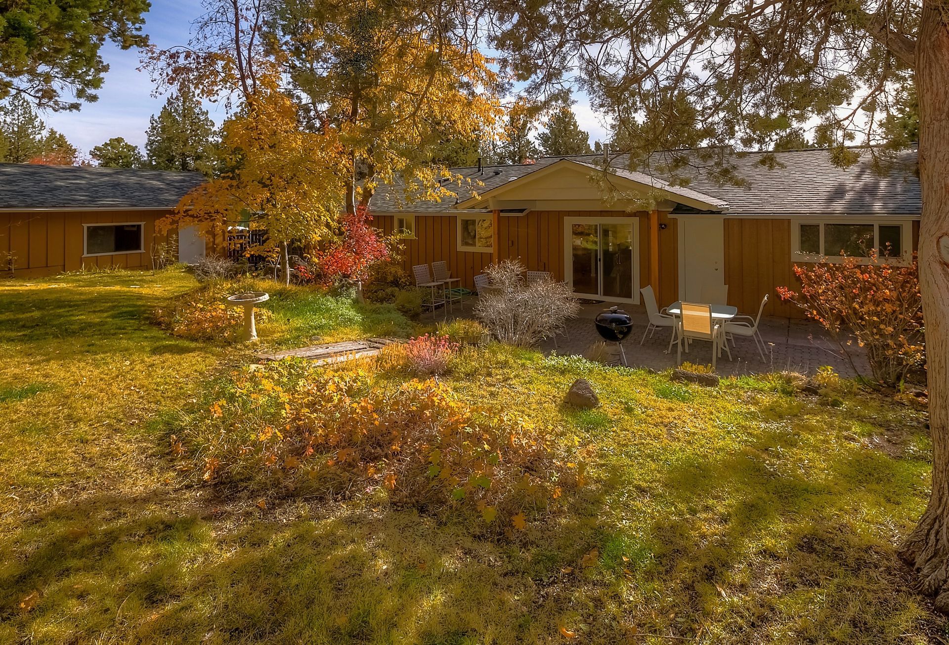 Backyard view of a house with fall foliage and a patio set.