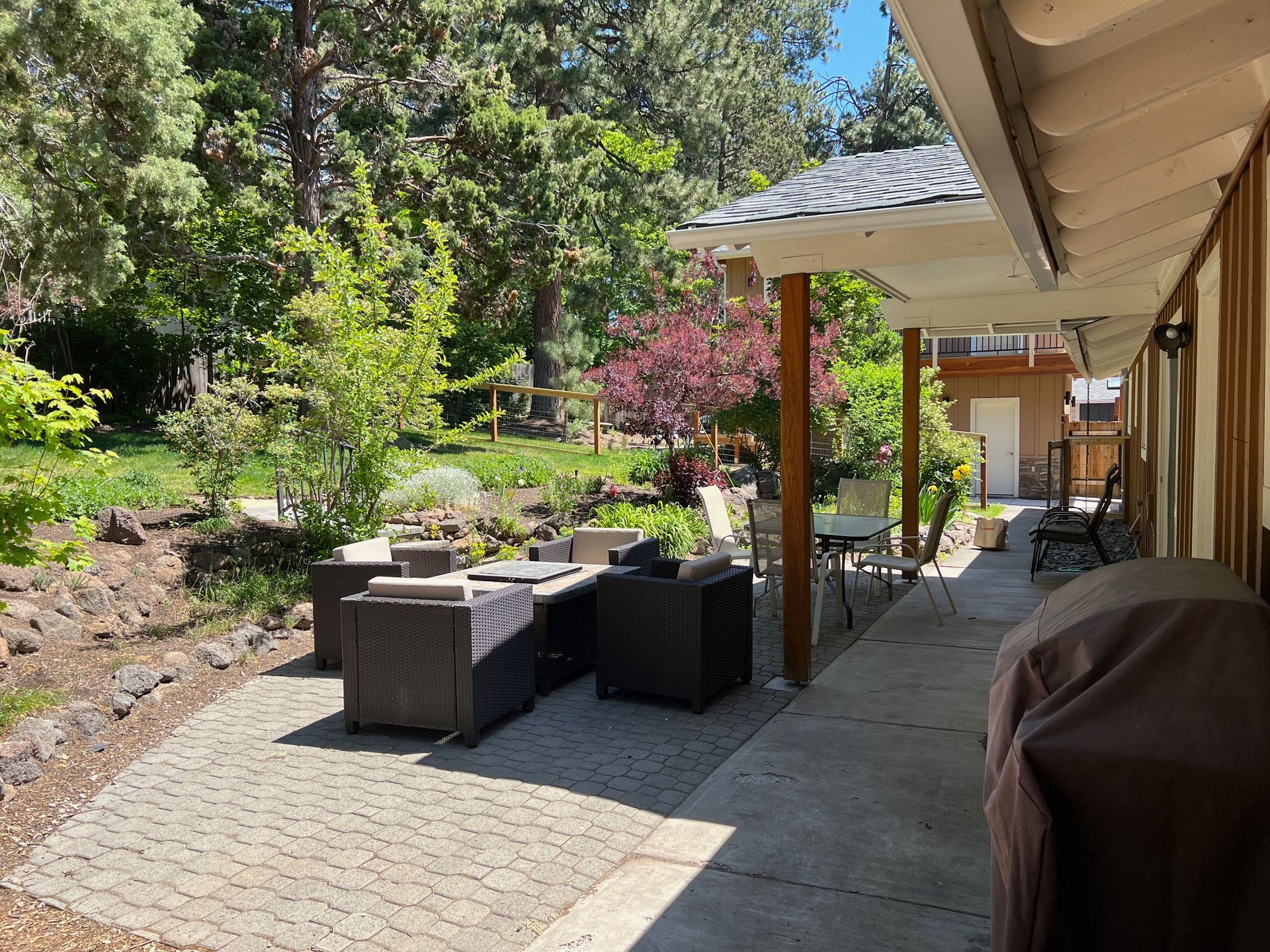 Patio with outdoor furniture, stone pavers, lush greenery, and a covered walkway.