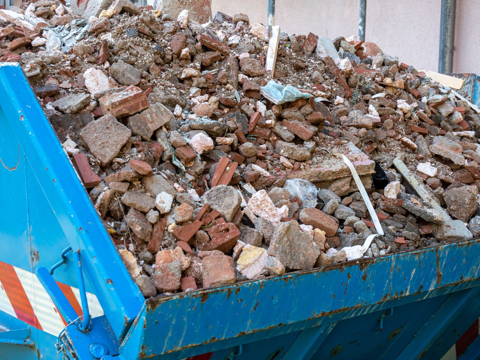 Blue dumpster overflowing with construction debris, including bricks and concrete.