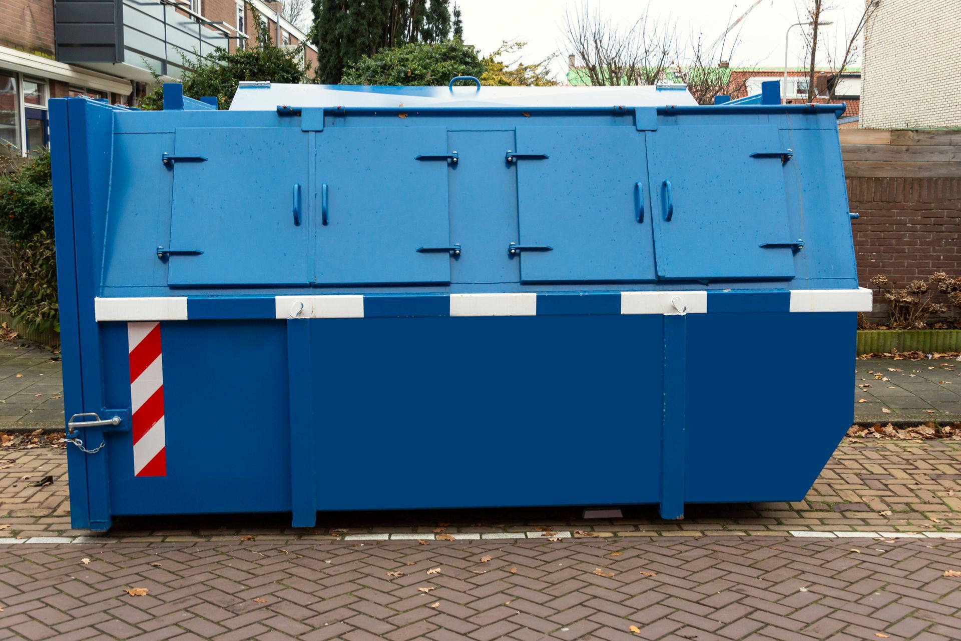Blue waste container with three compartments, on a brick sidewalk.