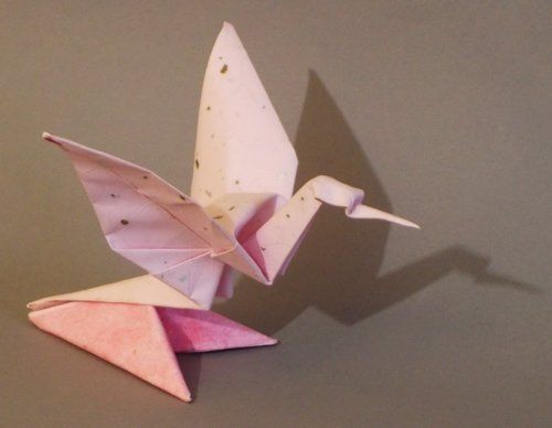 Photo of an pale pink origami peace crane on a darker pink stand