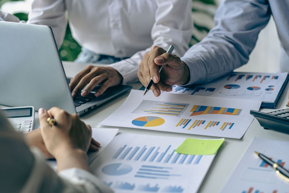 People reviewing financial reports on a table, including charts, laptop, and calculator.