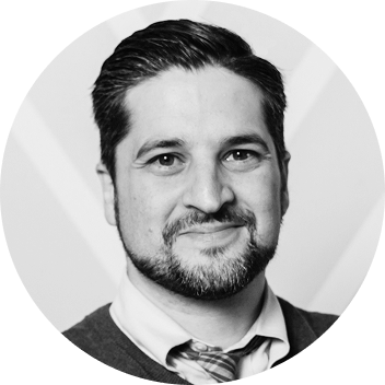 A man with a beard and tie is smiling in a black and white photo.