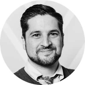 A man with a beard and tie is smiling in a black and white photo.