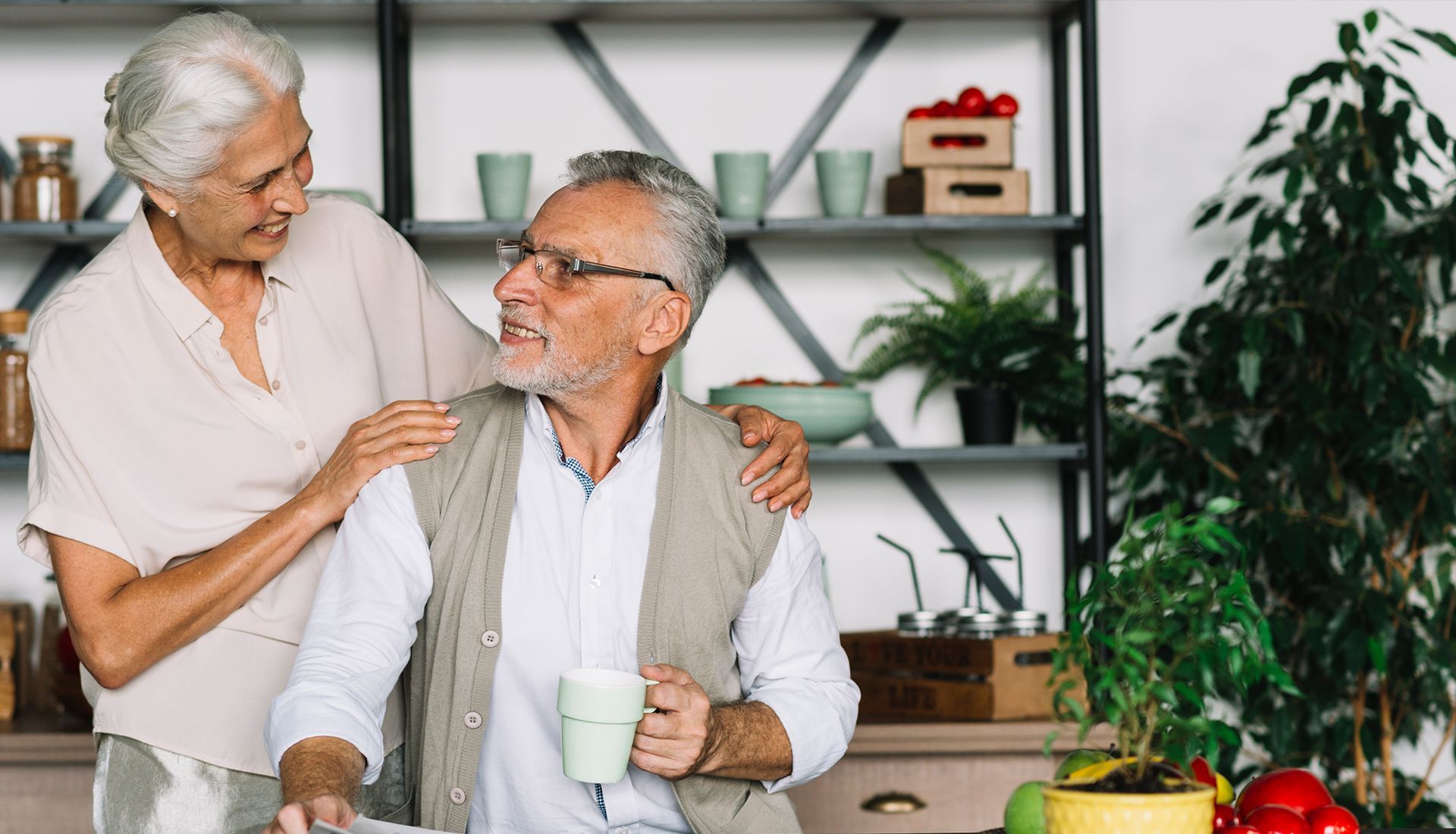 An elderly couple is standing next to each other in a kitchen.