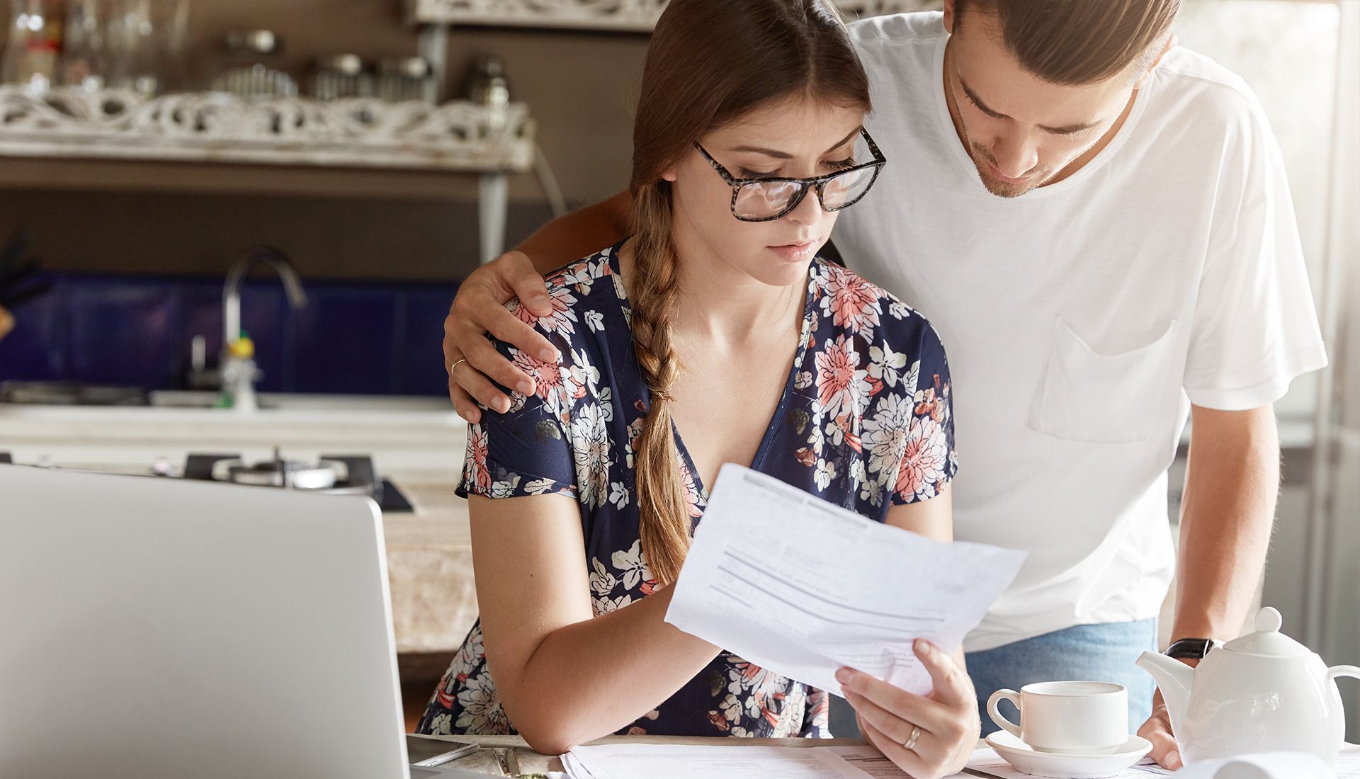 A man and a woman are looking at a piece of paper in front of a laptop.