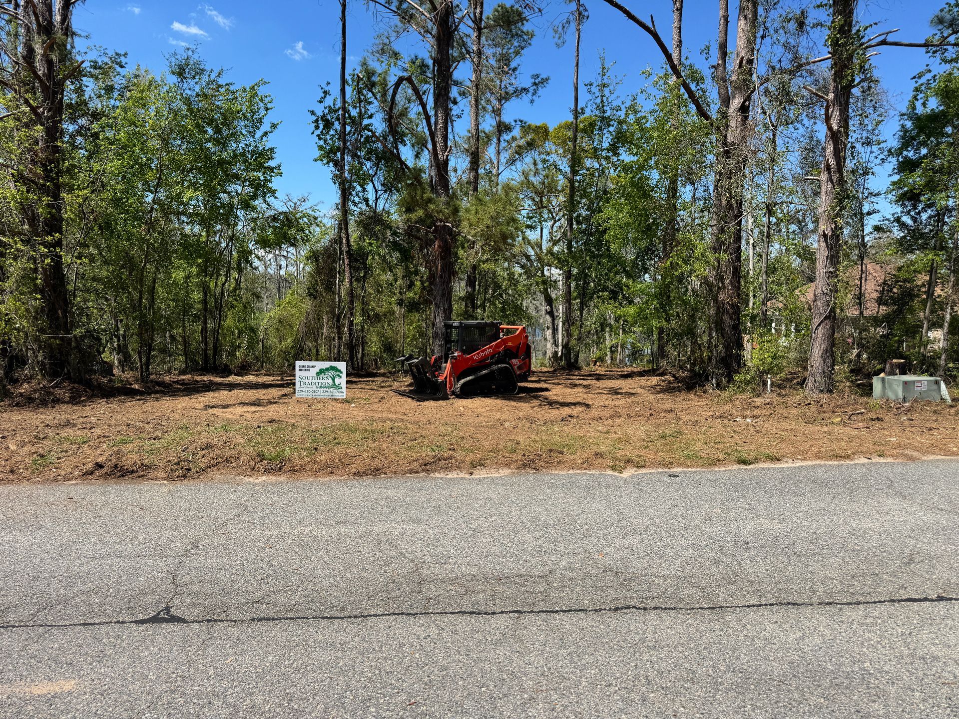 A red bulldozer is parked on the side of a road next to a forest.
