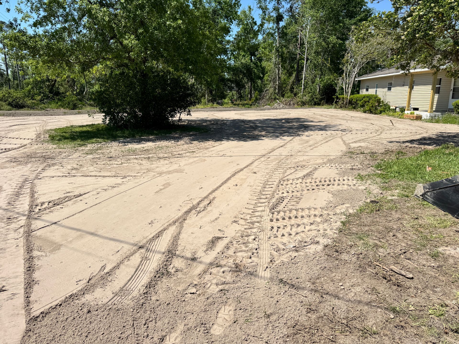 A dirt road leading to a house with trees in the background.