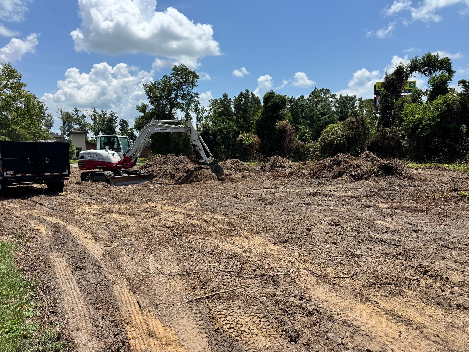 An excavator is working on a dirt field with trees in the background.