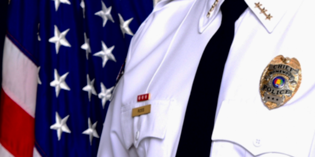 A police officer stands in front of an american flag