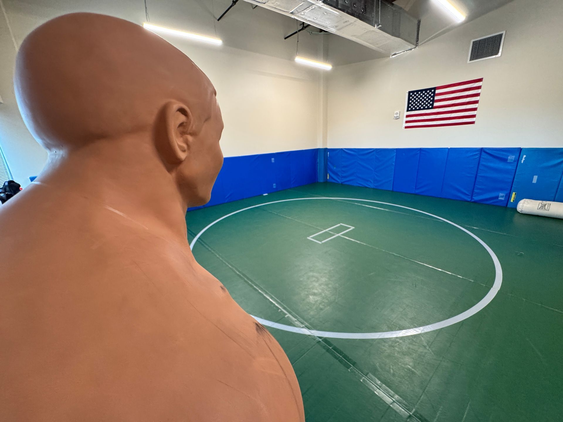 A mannequin is standing in a wrestling ring in a gym.
