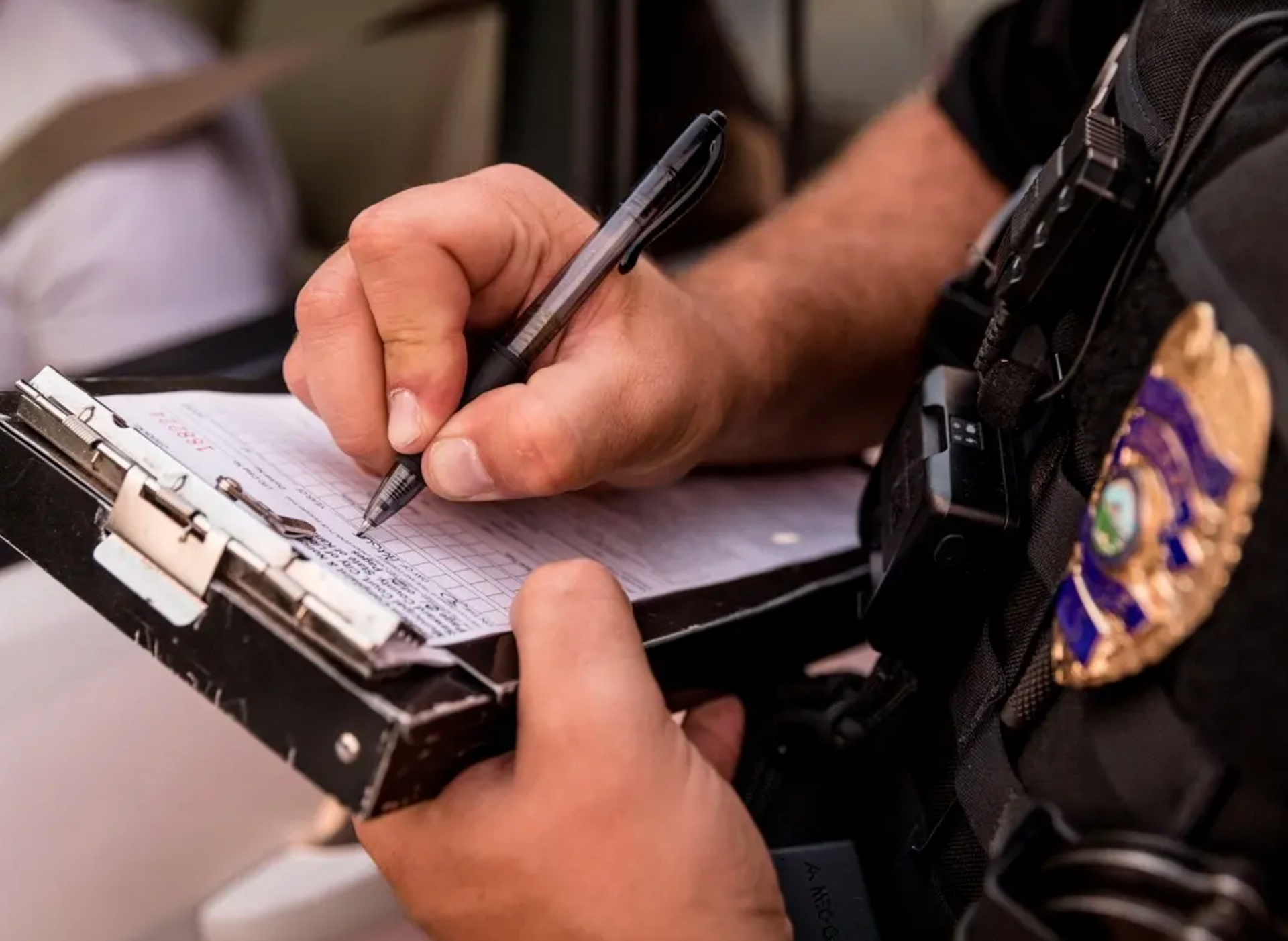 A police officer is writing on a clipboard with a pen.