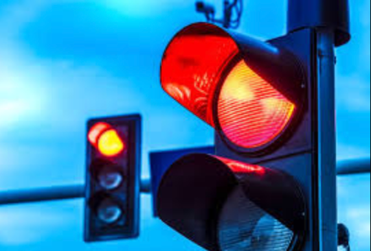 A close up of a red traffic light with a blue sky in the background.