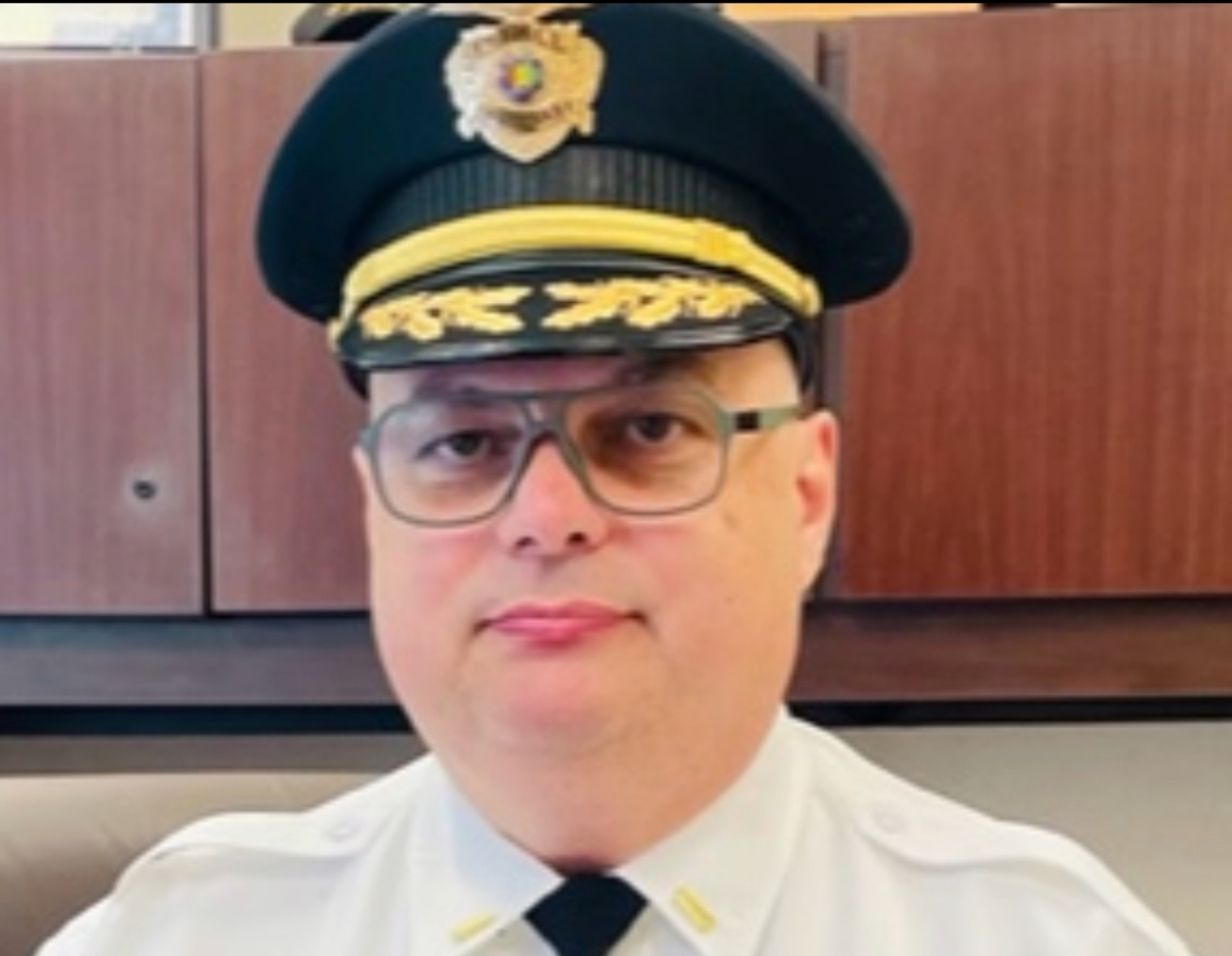 A police officer wearing a hat and glasses looks at the camera