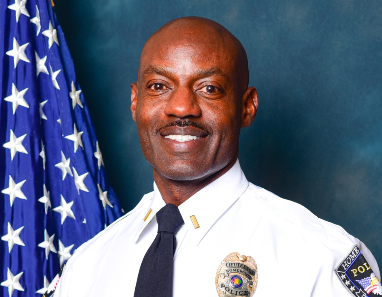 A man in a police uniform stands in front of an american flag