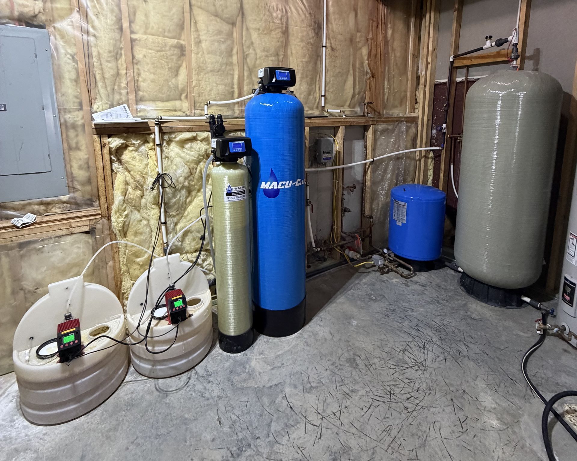 A residential water treatment system in a basement featuring two large tanks, two smaller units, and two chemical pumps.