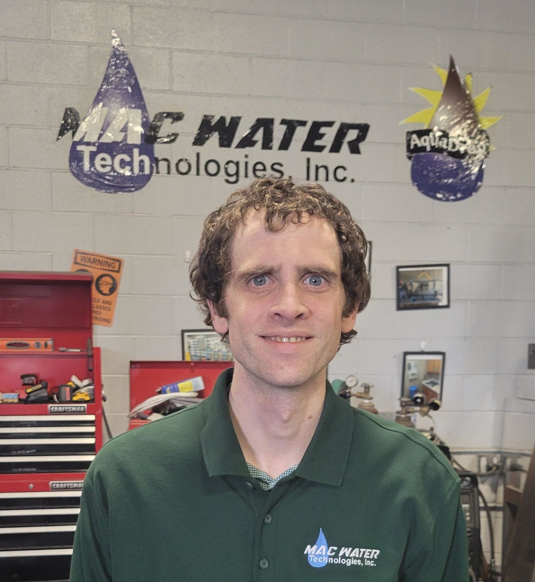A man in a green shirt is standing in front of a wall that says mac water technologies inc.