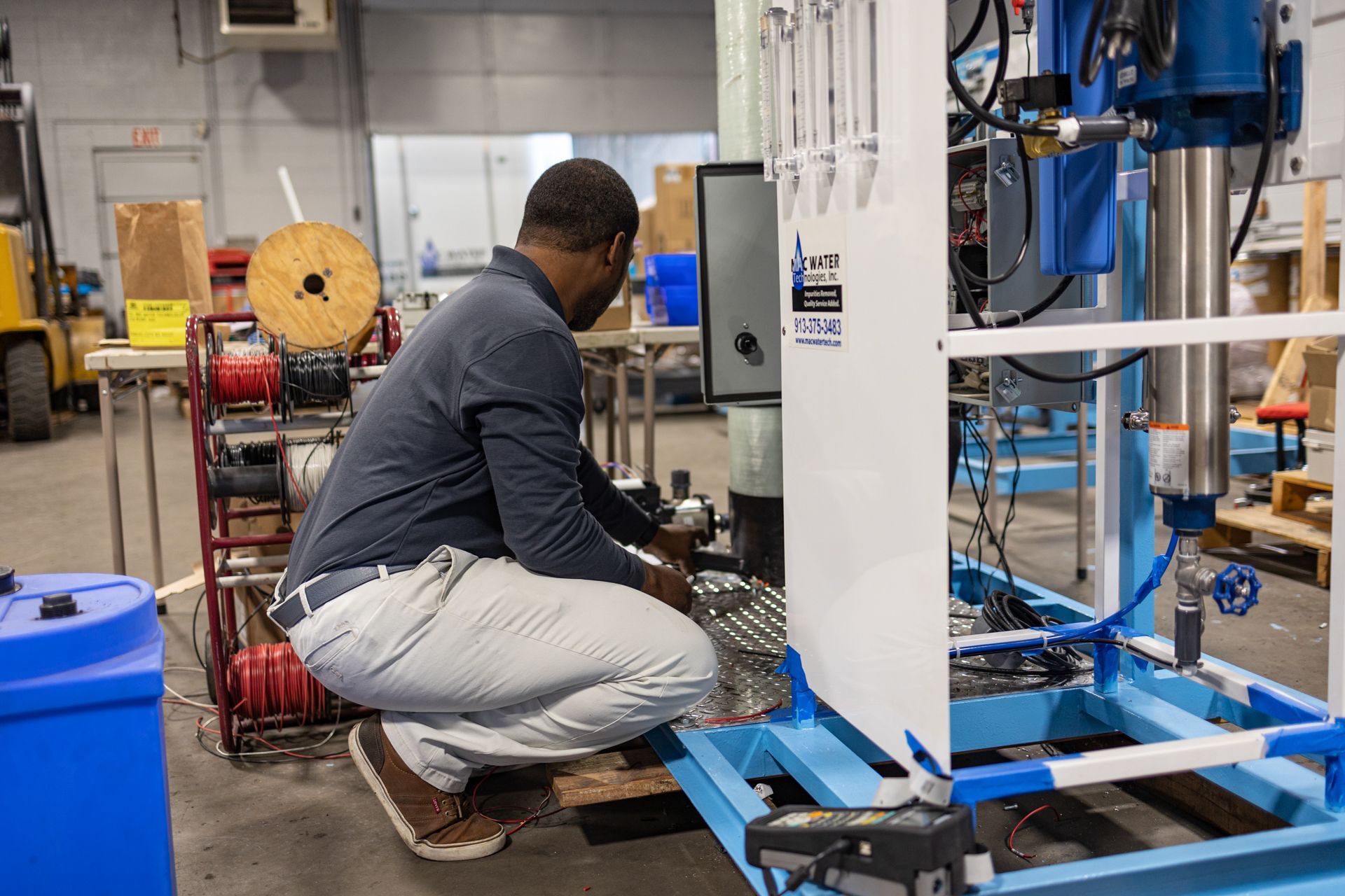 A man is kneeling down in front of a machine in a factory.