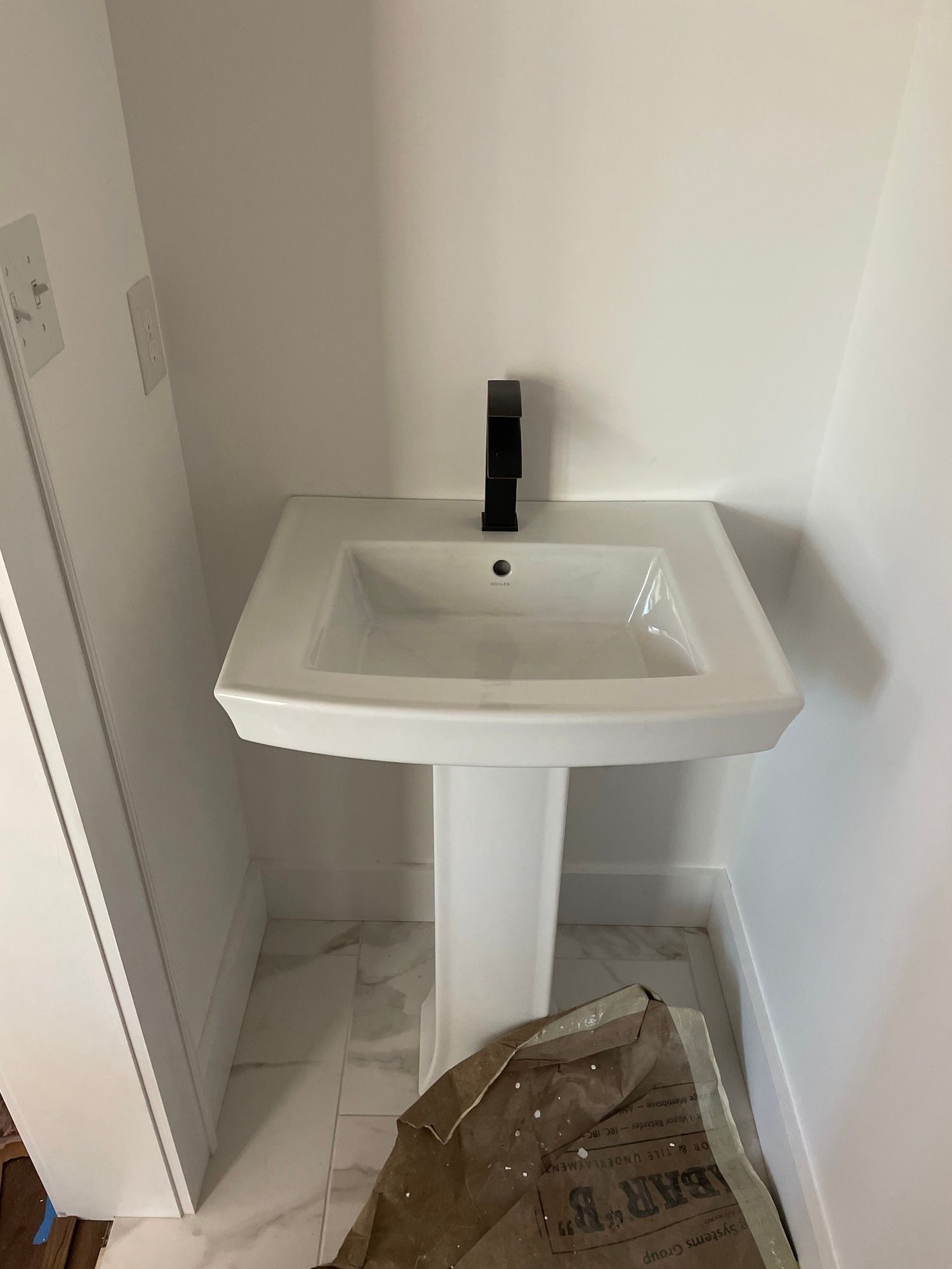 A white pedestal sink with a black faucet in a bathroom.