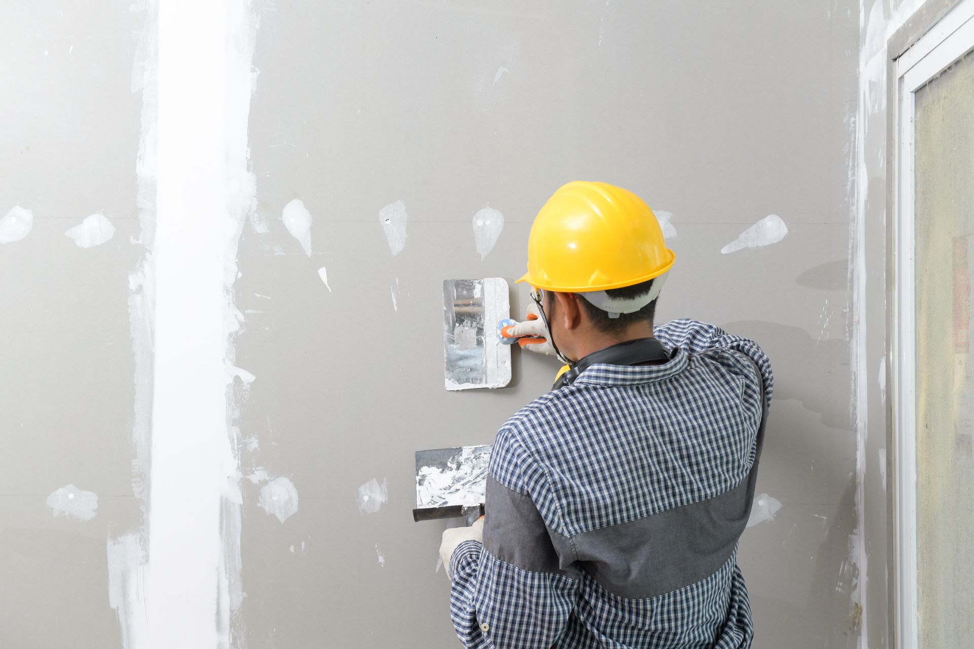 A man in a hard hat is plastering a wall.