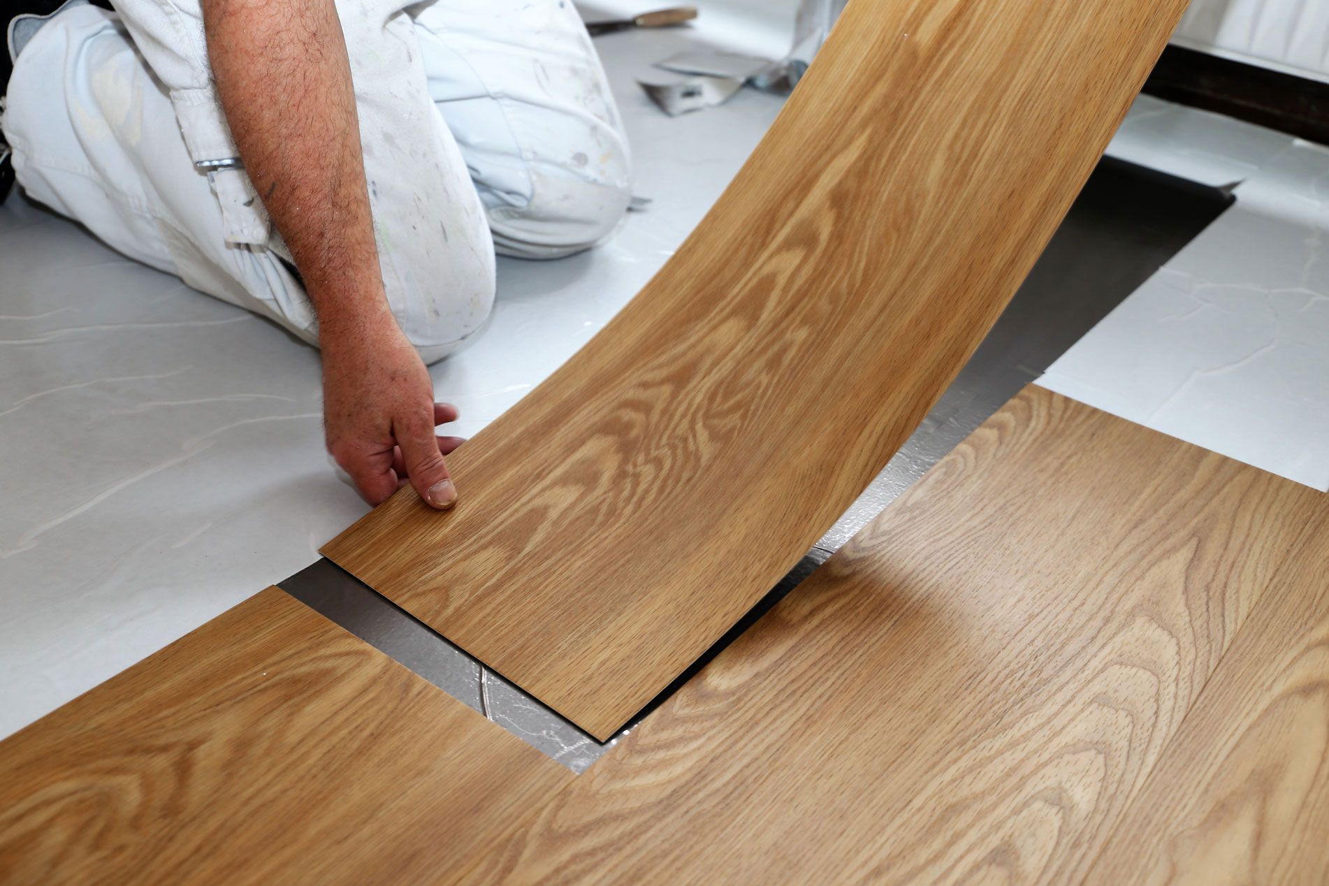A man is laying a piece of vinyl flooring on the floor.